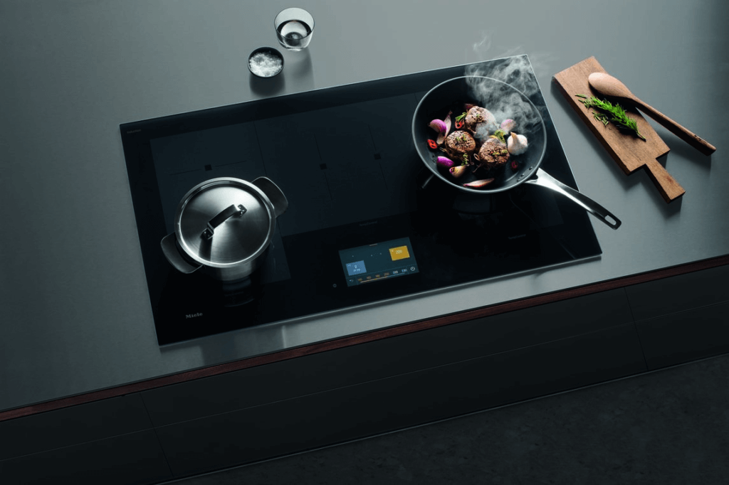A pot of food and pan of steak on a beautiful Miele induction cooktop