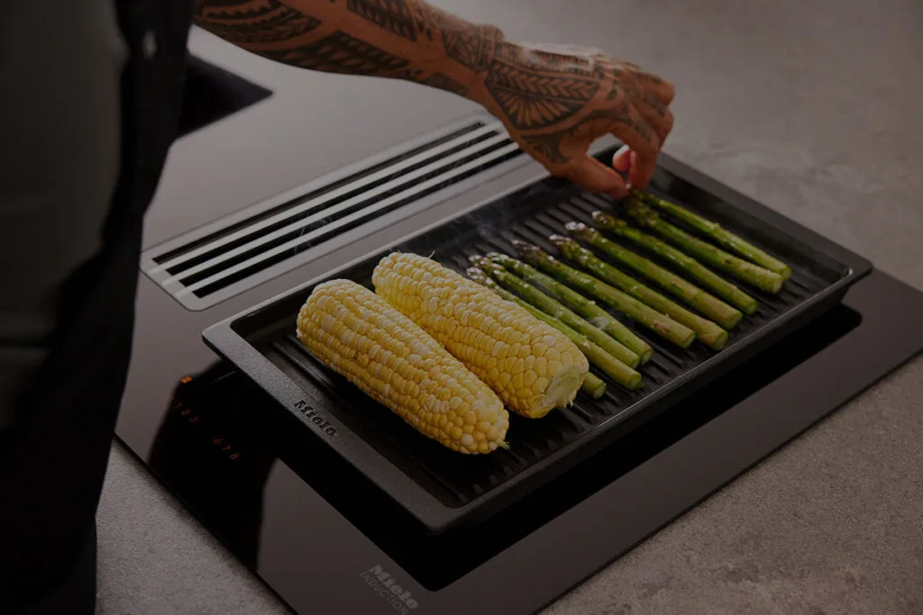 Corn on the cob and asparagus being grilled on a Miele cooktop