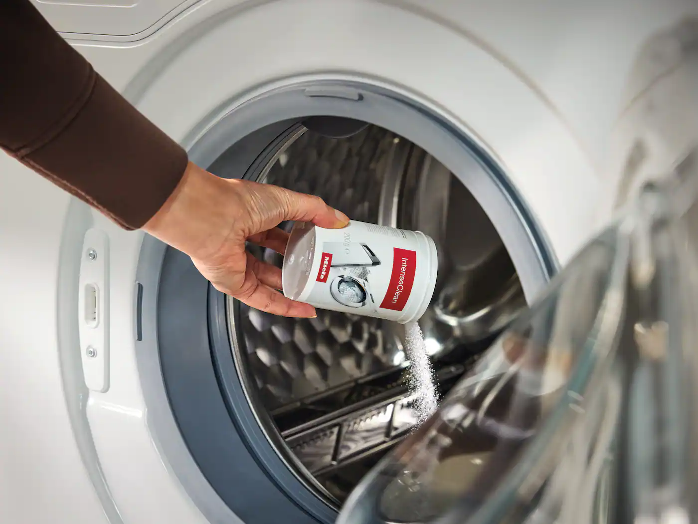 A person sprinkling Miele IntenseClean into a Miele washing machine