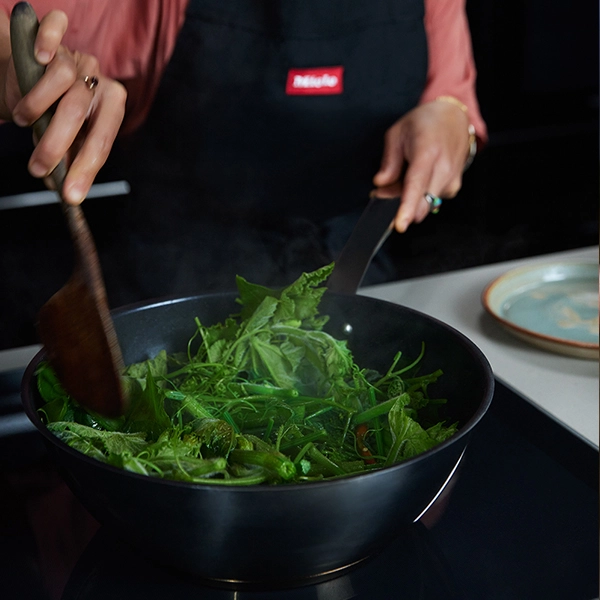 Green vegetables being stir-fried in a wok on a Miele induction cooktop